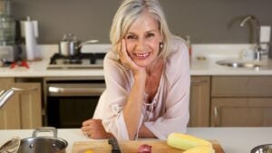 Vrouw glimlacht vriendelijk in moderne keuken met verse groenten, klaar voor koken of een gezonde maaltijd.